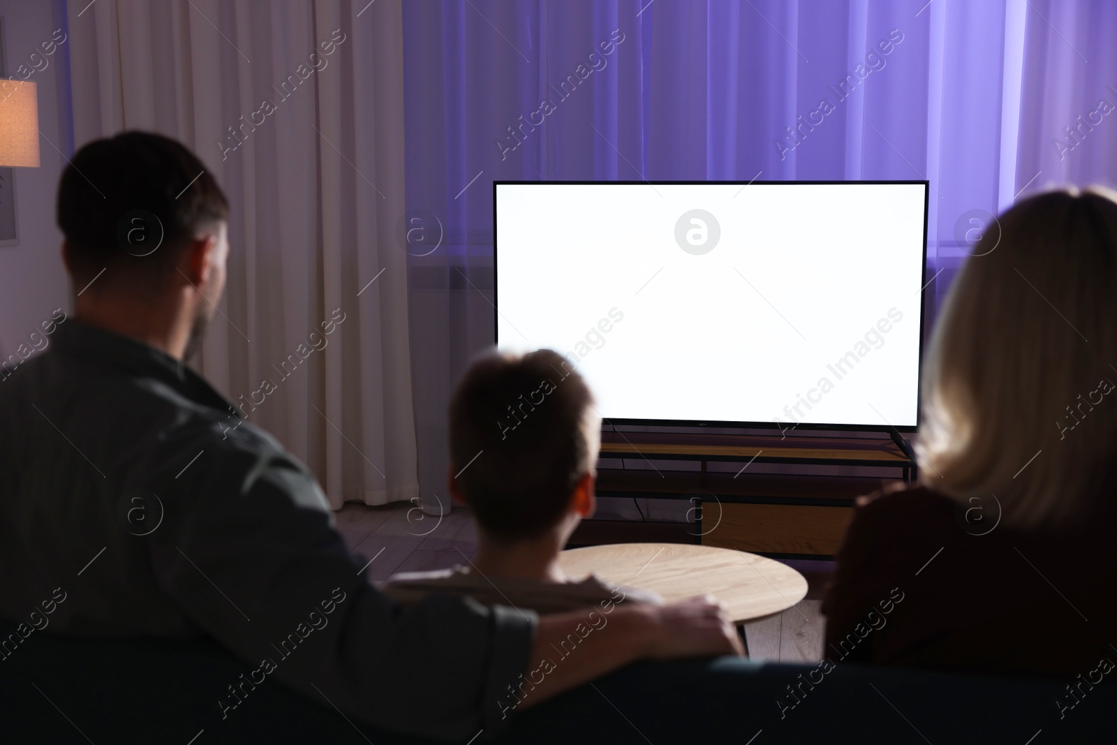 Photo of Happy family watching tv together at home in evening, back view