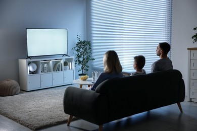 Happy family with snacks and drinks watching tv together at home