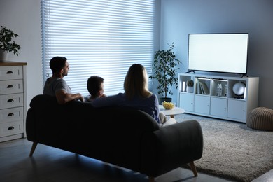 Photo of Happy family with snacks and drinks watching tv together at home