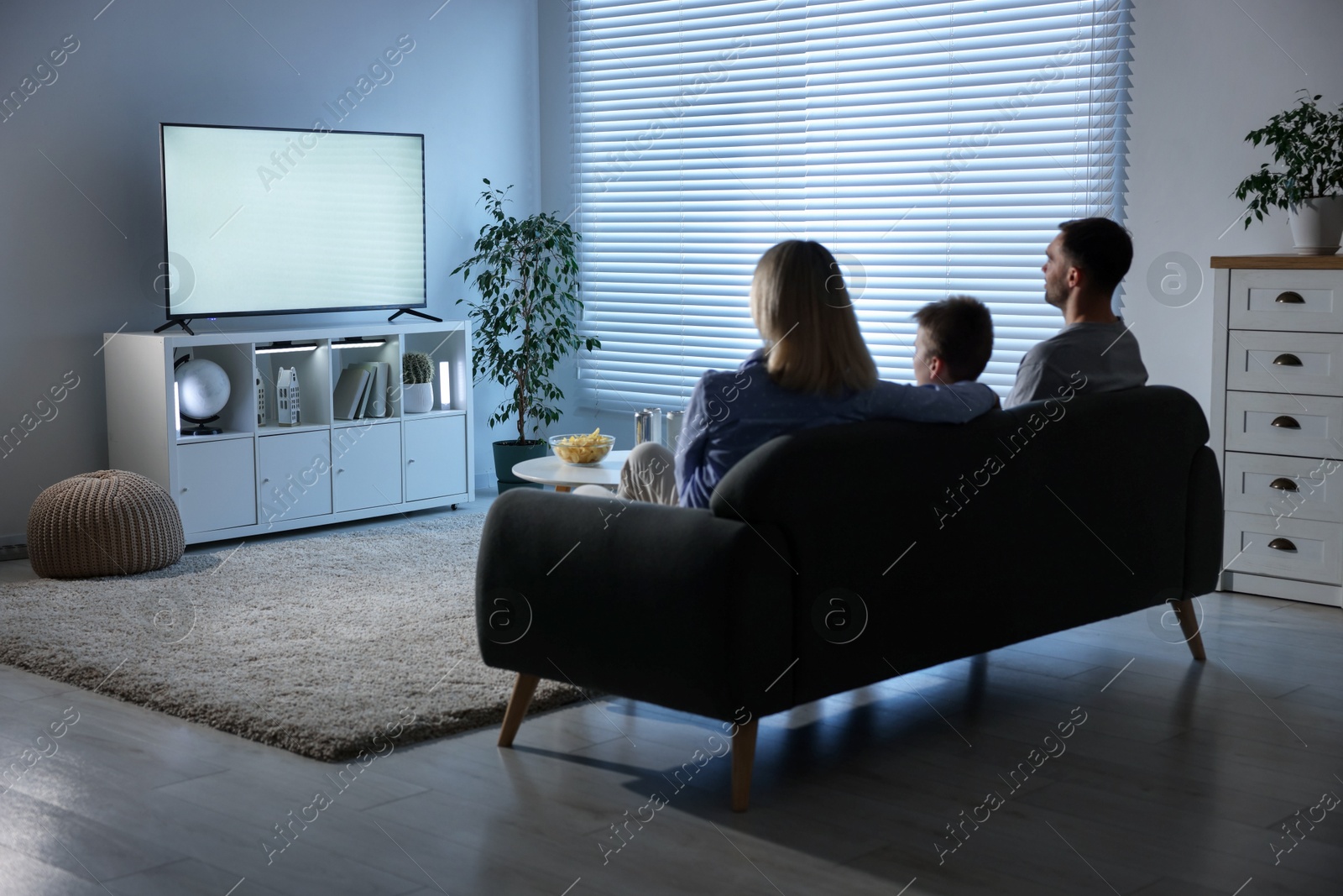 Photo of Happy family with snacks and drinks watching tv together at home