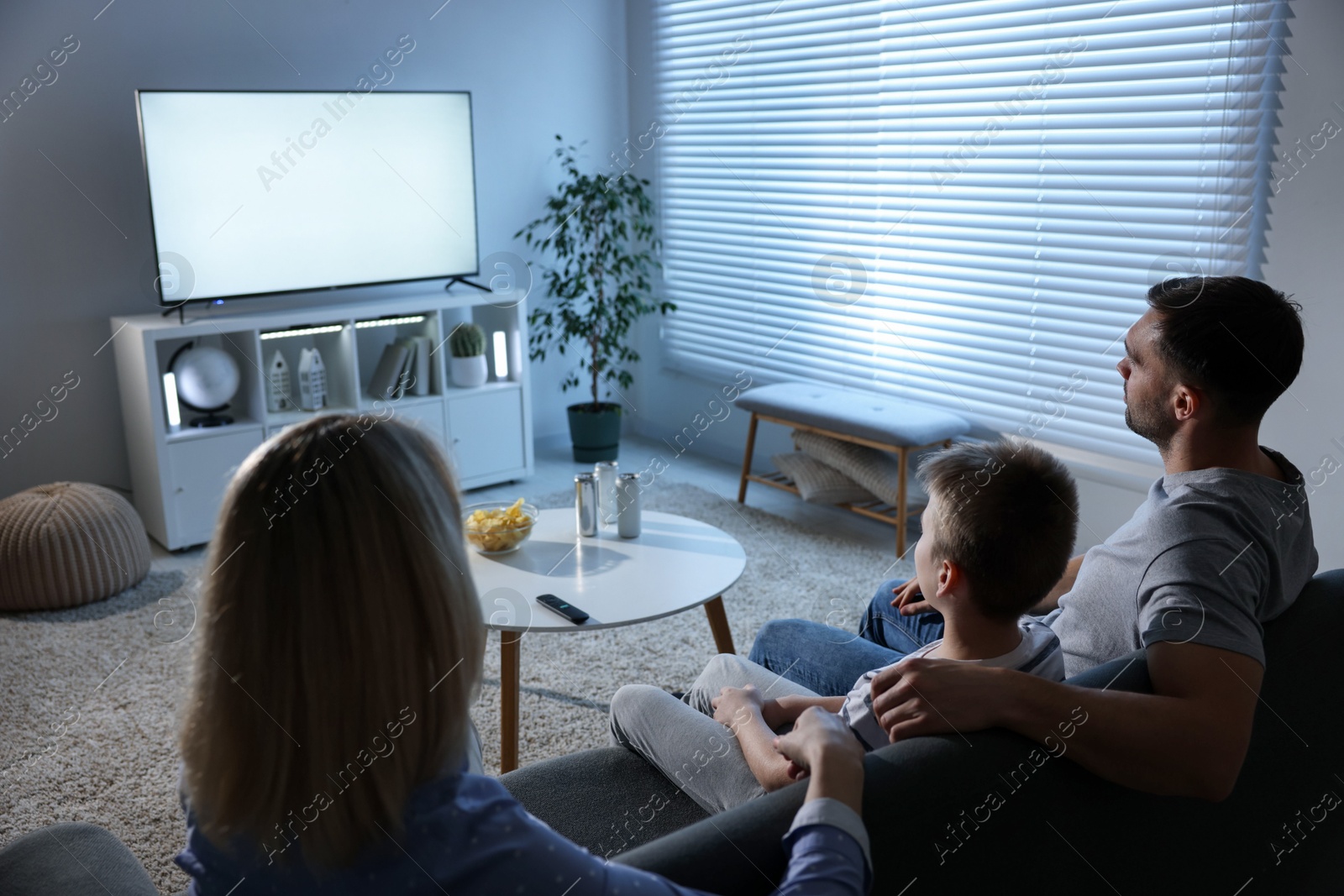 Photo of Happy family with snacks and drinks watching tv together at home