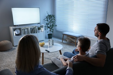 Happy family with snacks and drinks watching tv together at home