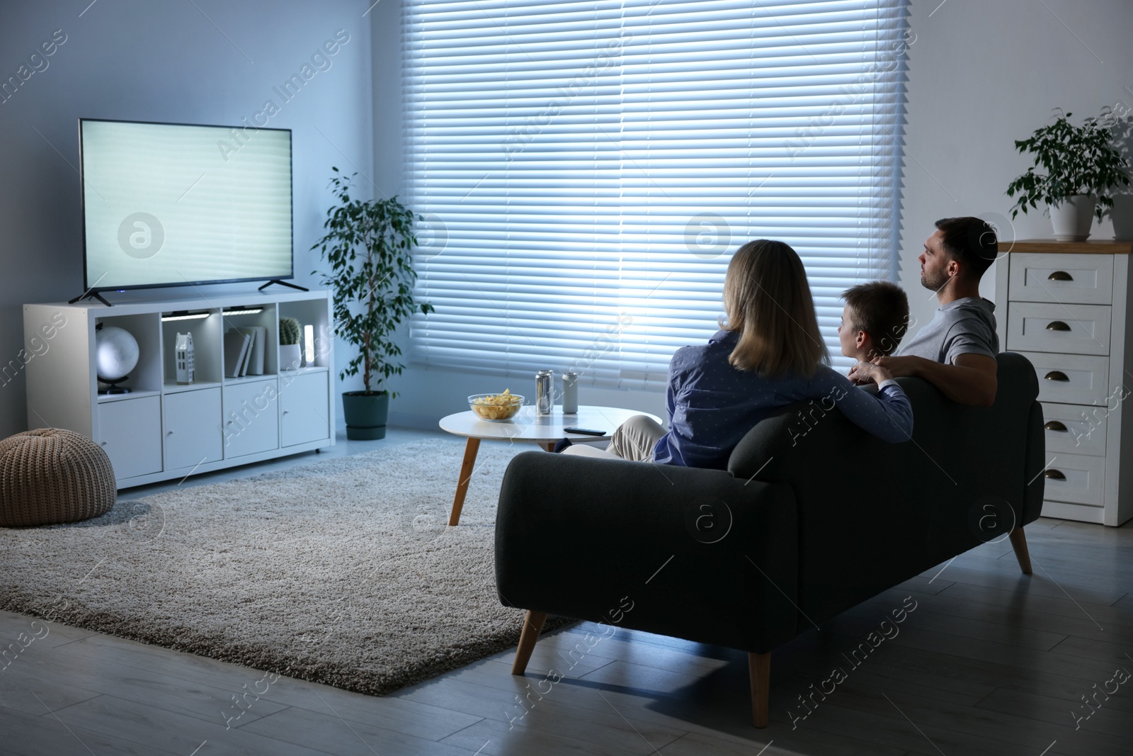 Photo of Happy family with snacks and drinks watching tv together at home