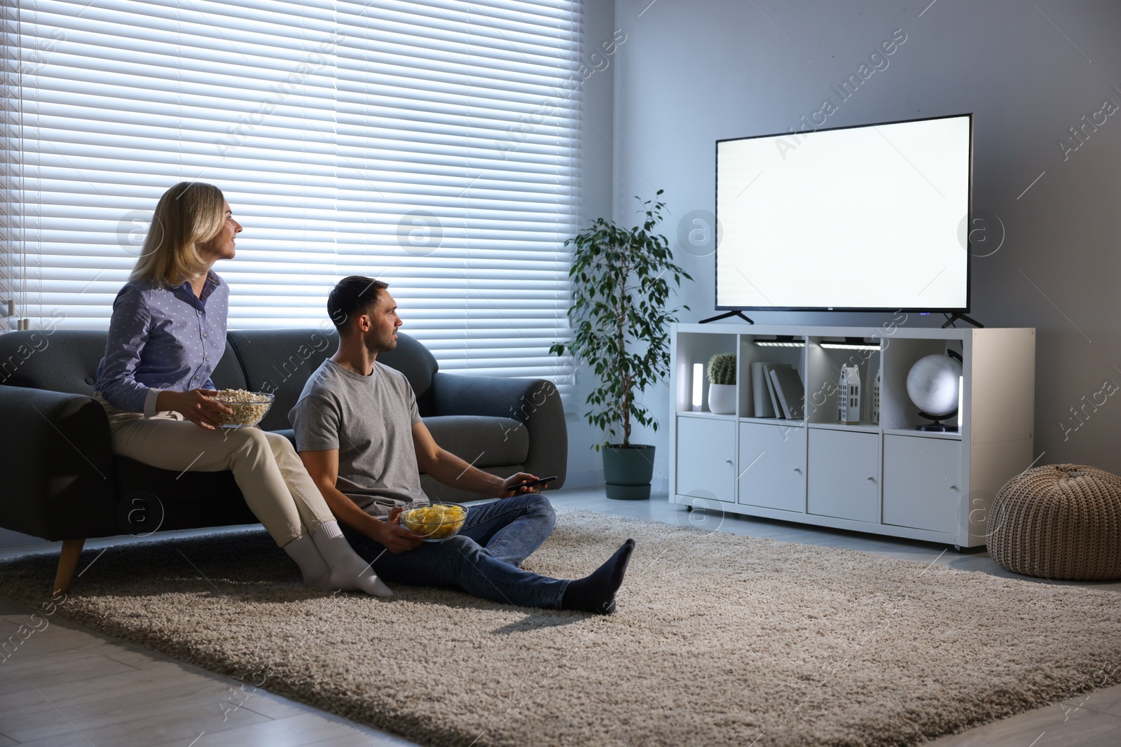 Photo of Lovely couple with snacks watching tv at home