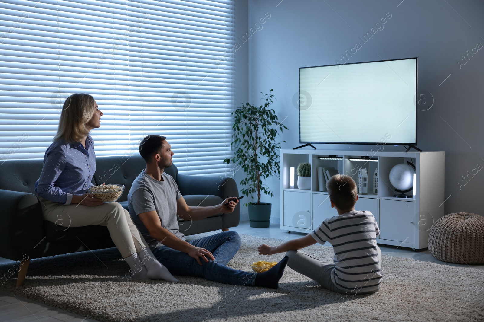 Photo of Happy family with snacks watching tv together at home