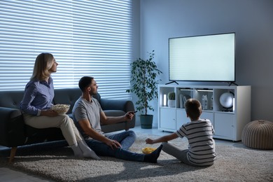 Happy family with snacks watching tv together at home