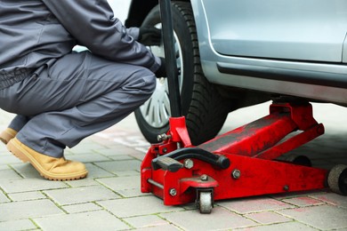 Photo of Car lifted by scissor jack. Auto mechanic changing wheel outdoors, closeup