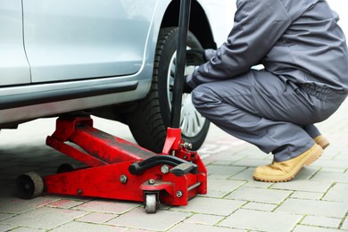 Photo of Car lifted by scissor jack. Auto mechanic changing wheel outdoors, closeup