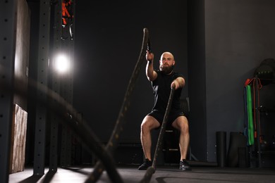 Photo of Sportsman exercising with battle ropes during crossfit workout in gym