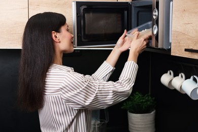 Photo of Woman putting container with lunch into microwave indoors