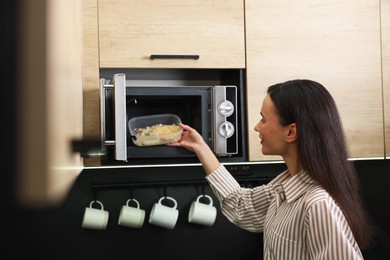 Photo of Woman putting container with lunch into microwave indoors