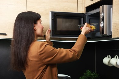 Photo of Woman putting container with lunch into microwave indoors