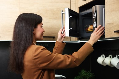 Photo of Woman putting container with lunch into microwave indoors