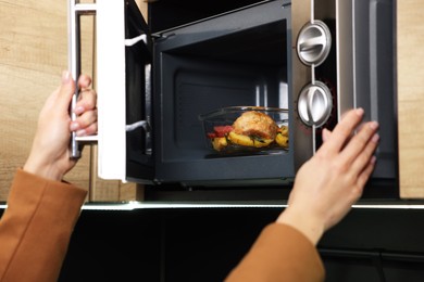 Photo of Woman putting container with lunch into microwave indoors, closeup