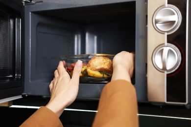 Photo of Woman putting container with lunch into microwave indoors, closeup