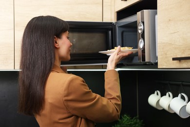 Photo of Woman putting plate with lunch into microwave indoors