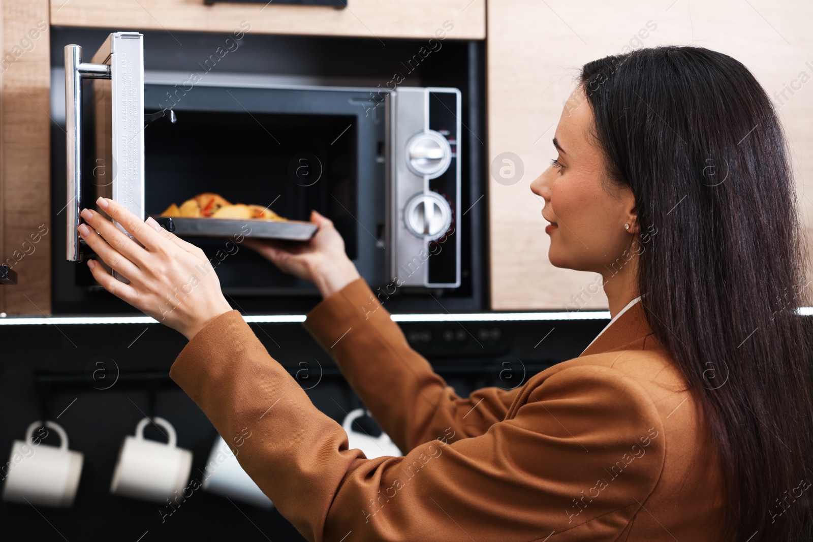 Photo of Woman putting plate with lunch into microwave indoors