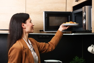 Photo of Woman putting plate with lunch into microwave indoors