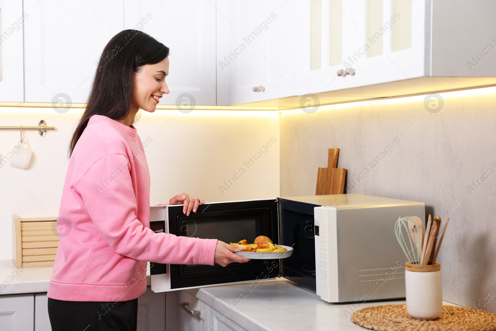 Photo of Woman putting plate with lunch into microwave indoors