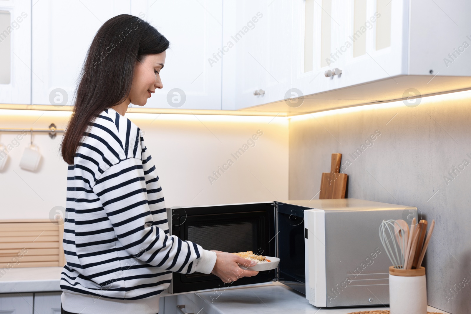 Photo of Woman putting plate with lunch into microwave indoors