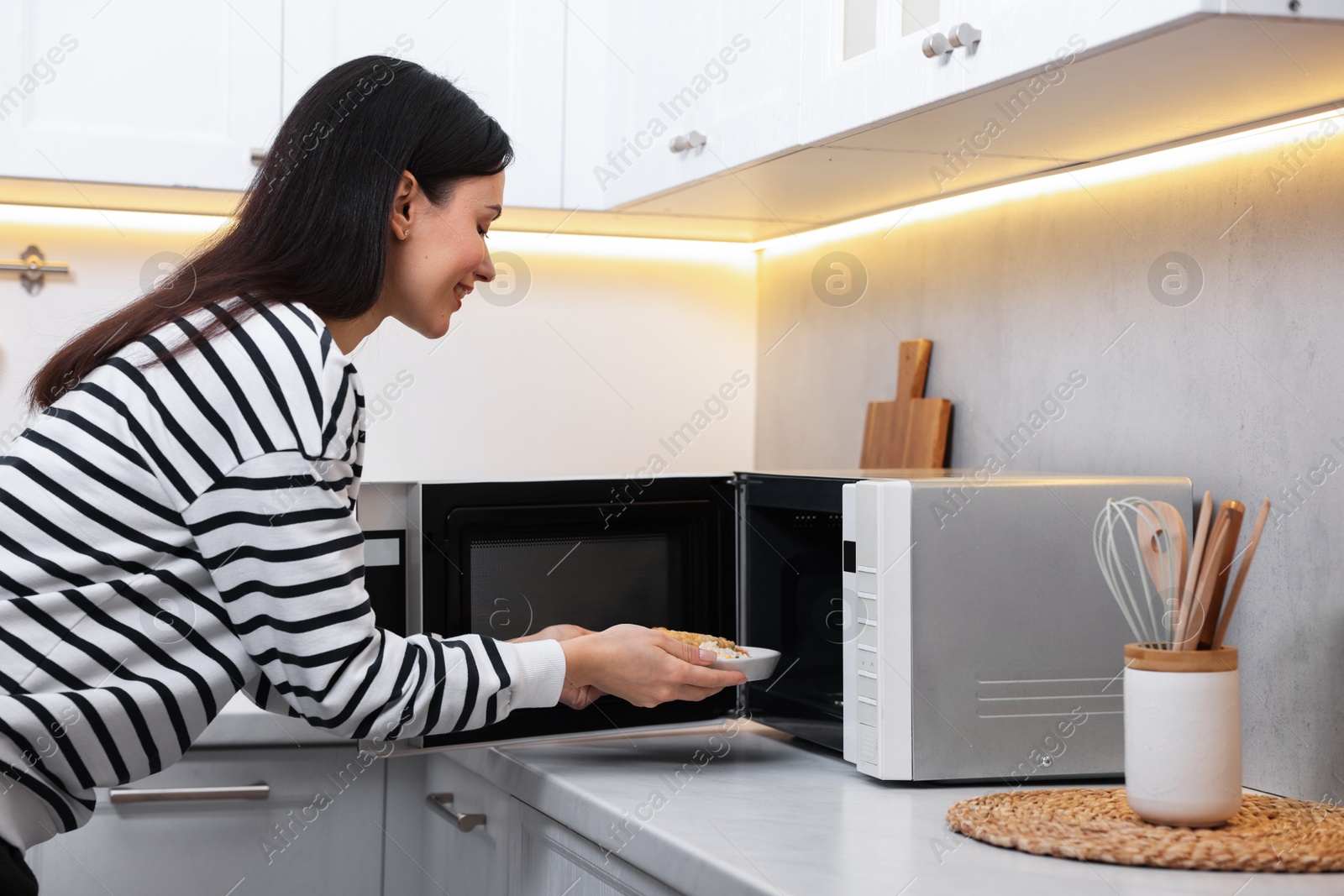 Photo of Woman putting plate with lunch into microwave indoors