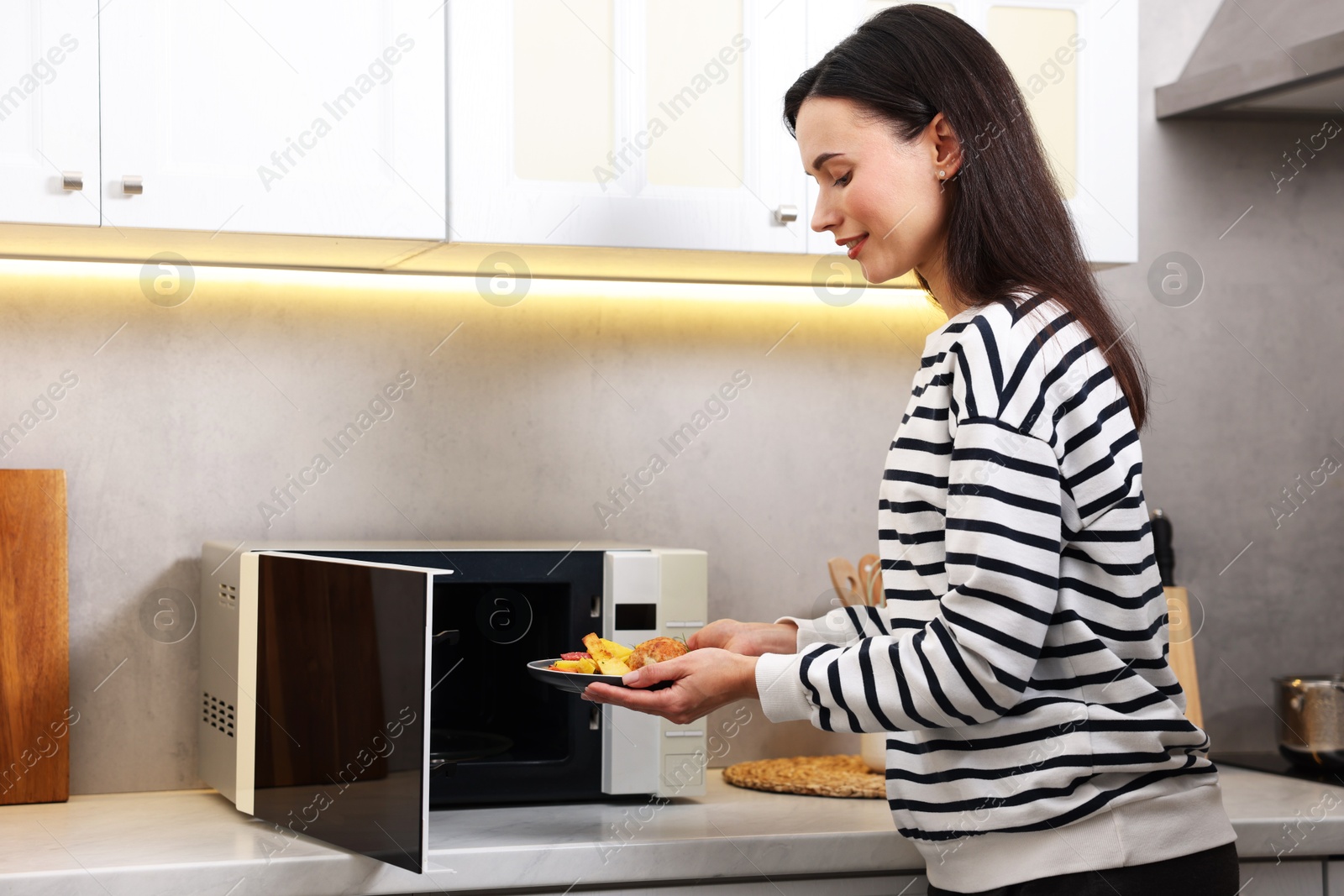 Photo of Woman putting plate with lunch into microwave indoors