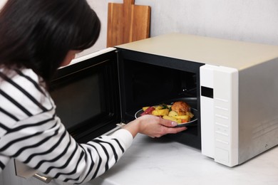 Photo of Woman putting plate with lunch into microwave indoors