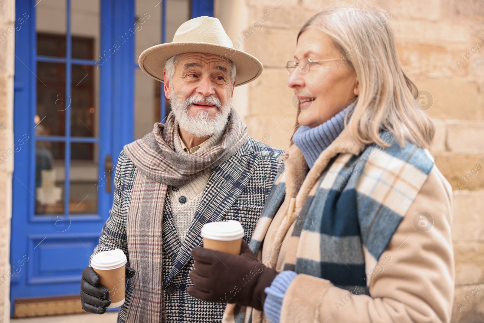 Photo of Happy elderly couple with coffee cups walking on city street