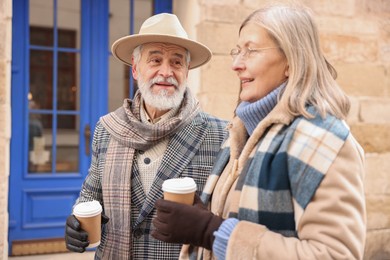 Happy elderly couple with coffee cups walking on city street