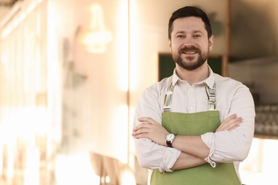 Photo of Portrait of smiling business owner with crossed arms in his cafe. Space for text