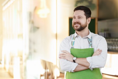 Photo of Portrait of smiling business owner with crossed arms in his cafe. Space for text