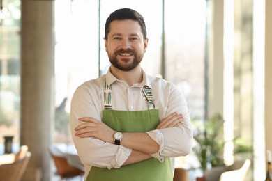 Portrait of smiling business owner with crossed arms in his cafe