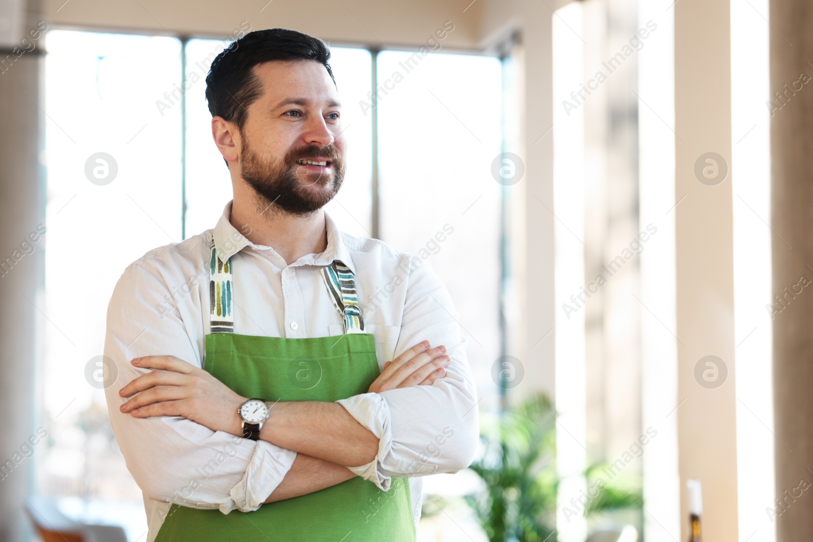 Photo of Smiling business owner with crossed arms in his cafe. Space for text