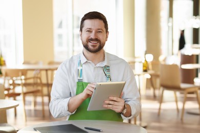 Smiling business owner with tablet in his cafe