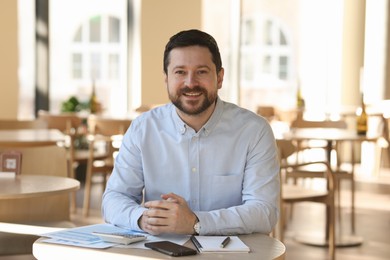 Photo of Portrait of smiling business owner at table in his cafe