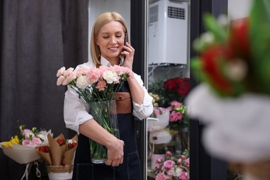 Photo of Business owner with beautiful carnations talking on smartphone in her flower shop