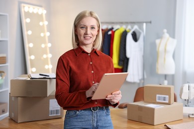 Photo of Business owner using tablet near table with parcels in her tailor shop