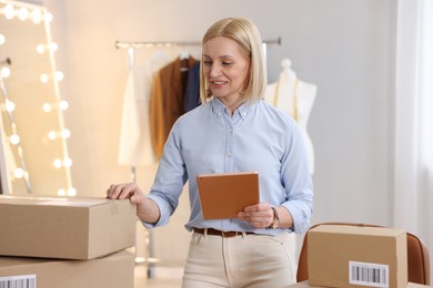 Photo of Business owner using tablet near parcels in her tailor shop