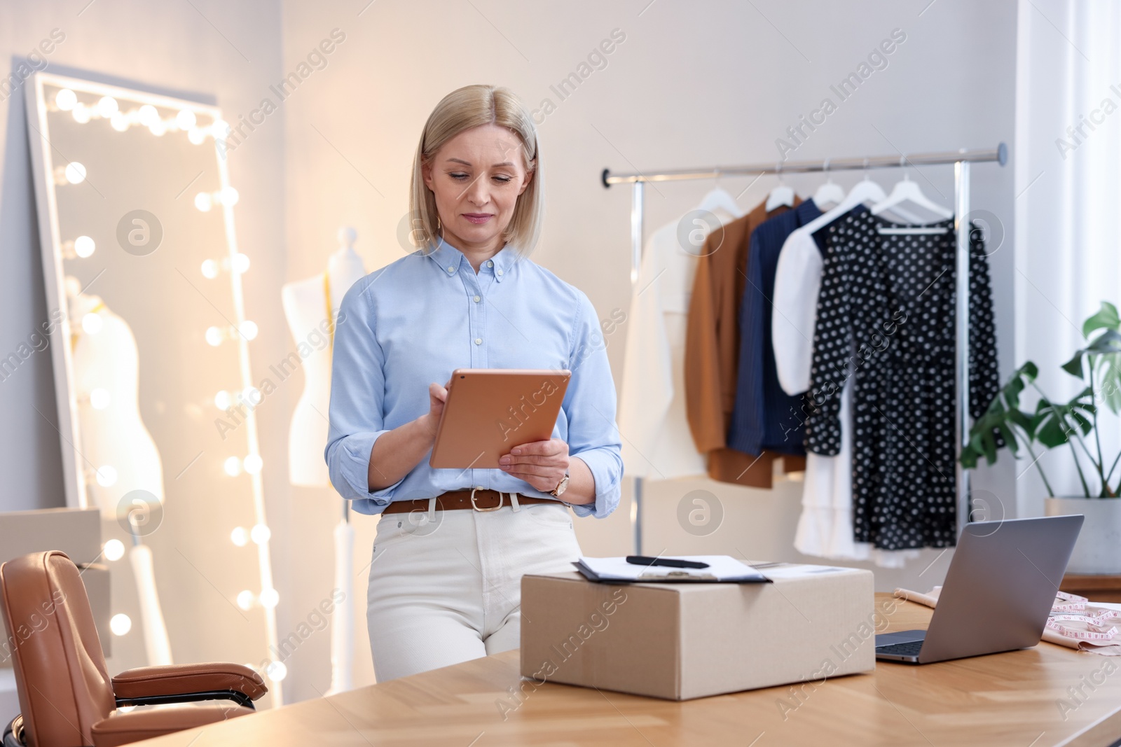 Photo of Business owner using tablet near table with parcel in her tailor shop