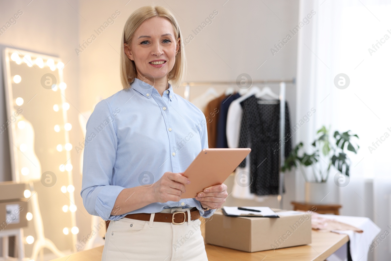 Photo of Business owner using tablet near table with parcel in her tailor shop, space for text