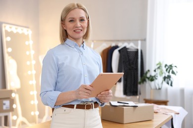 Business owner using tablet near table with parcel in her tailor shop, space for text