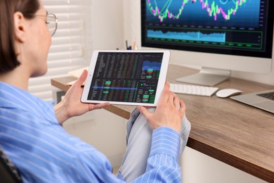 Photo of Stock exchange. Woman analysing financial market on tablet at wooden table indoors