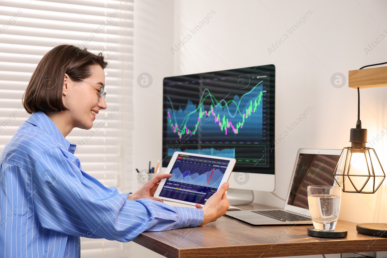 Photo of Stock exchange. Woman analysing financial market on tablet at wooden table indoors