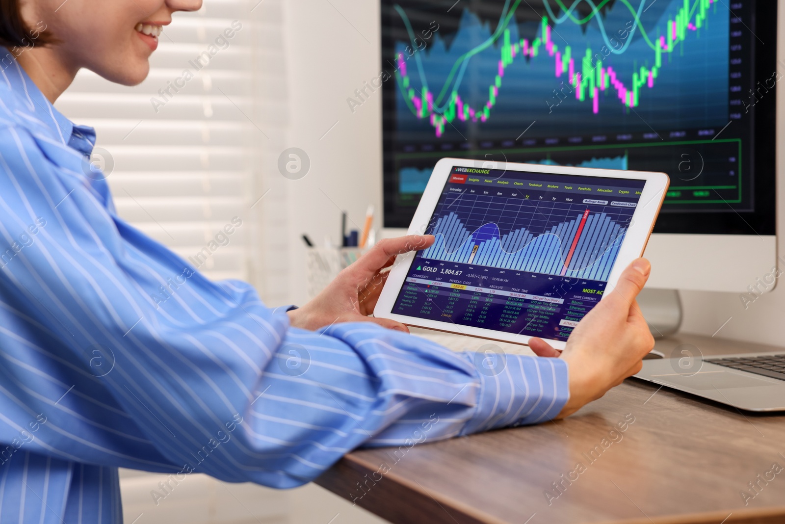 Photo of Stock exchange. Woman analysing financial market on tablet at wooden table indoors, closeup