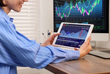 Stock exchange. Woman analysing financial market on tablet at wooden table indoors, closeup