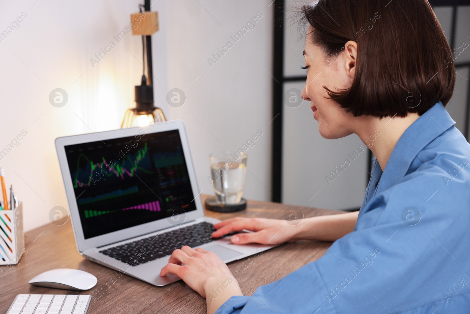 Photo of Stock exchange. Woman analysing financial market on laptop at wooden table indoors