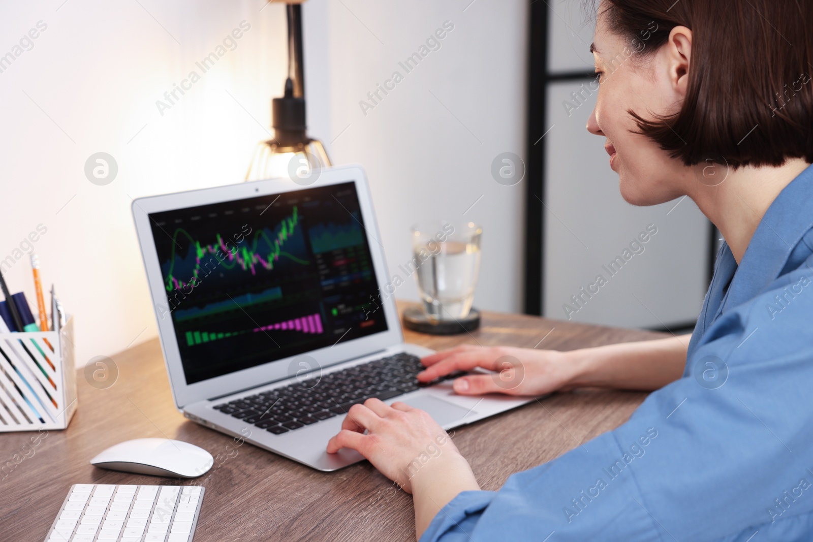 Photo of Stock exchange. Woman analysing financial market on laptop at wooden table indoors