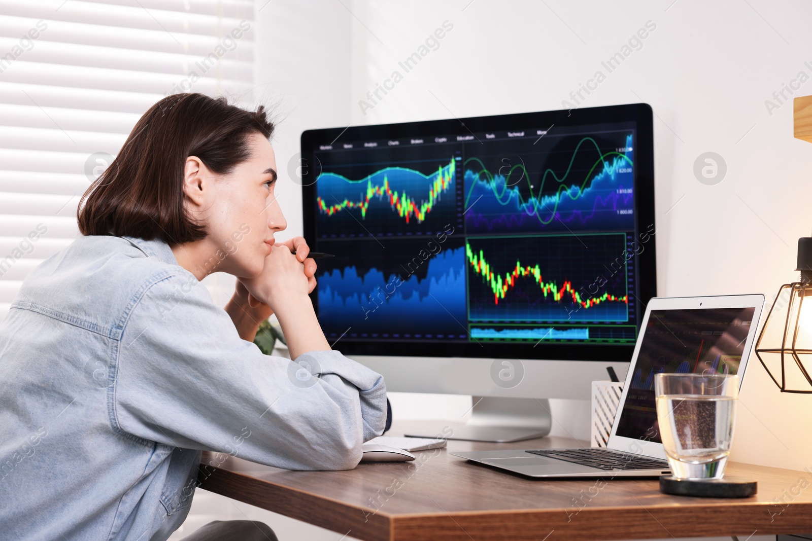 Photo of Stock exchange. Woman analysing financial market on computer at wooden table indoors