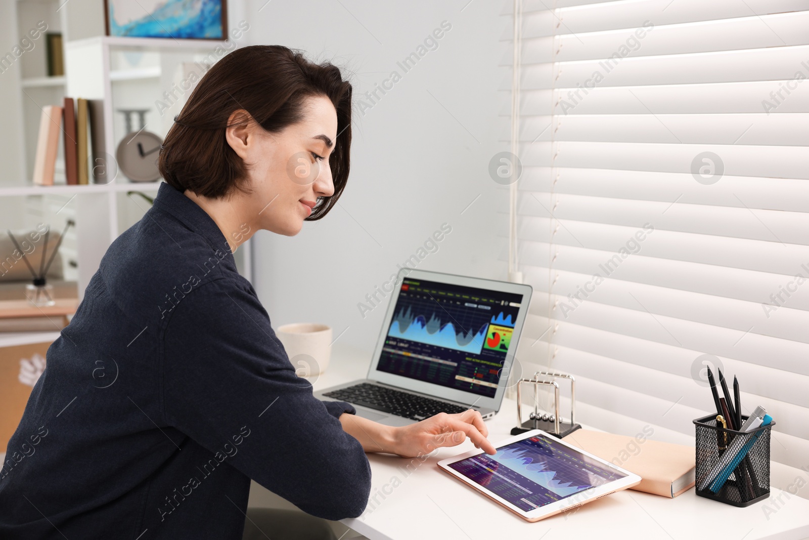 Photo of Stock exchange. Woman analysing financial market on tablet at white table indoors