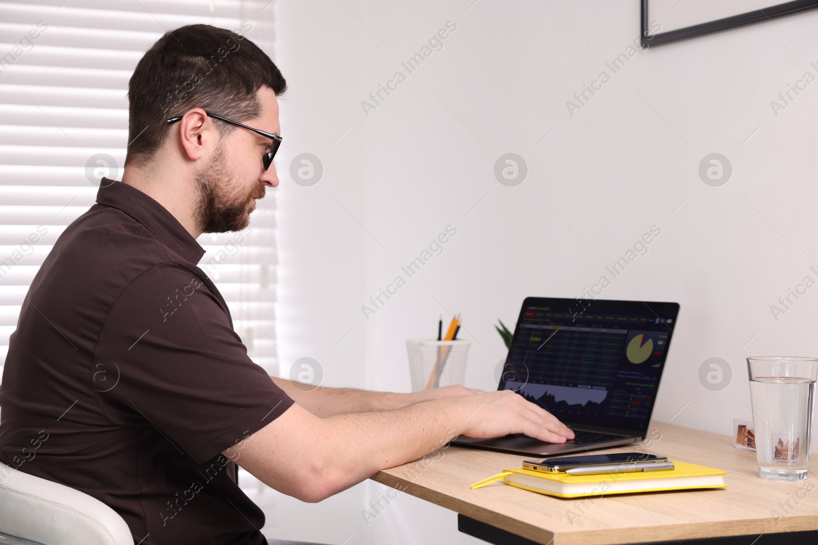 Photo of Stock exchange. Man analysing financial market on laptop at desk indoors